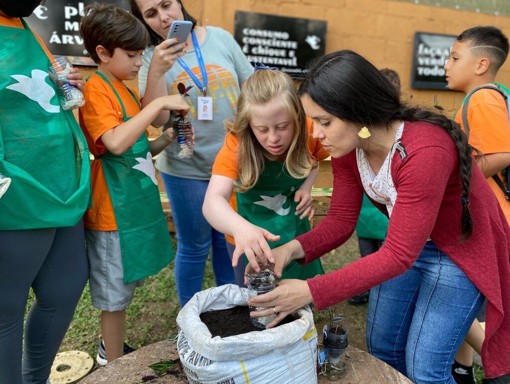 Aluna plantando uma muda em garrafa PET com ajuda da instrutora